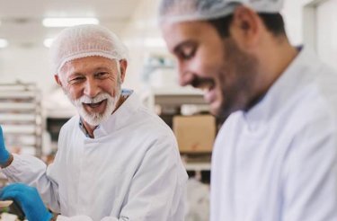 two-men-with-white-hats-in-lean-production-talking-and-laughing